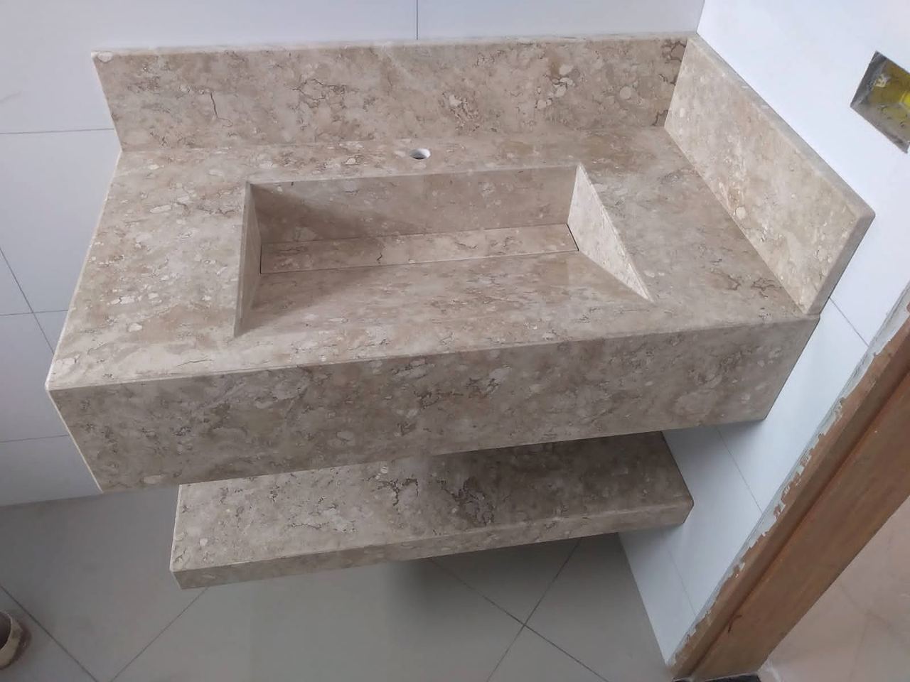 Lavatório com cuba esculpida em mármore bege e prateleira suspensa