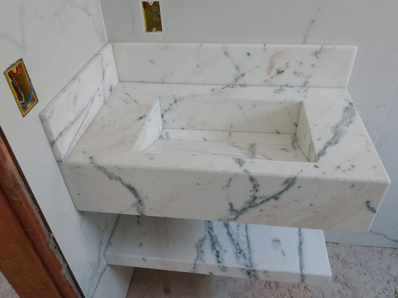 Lavatório com cuba esculpida em mármore branco de veios cinza e prateleira inferior