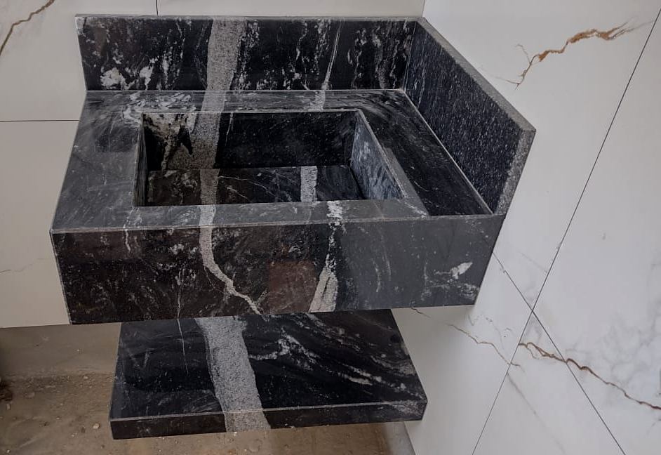 Lavatório com cuba esculpida em granito preto com veios brancos e prateleira